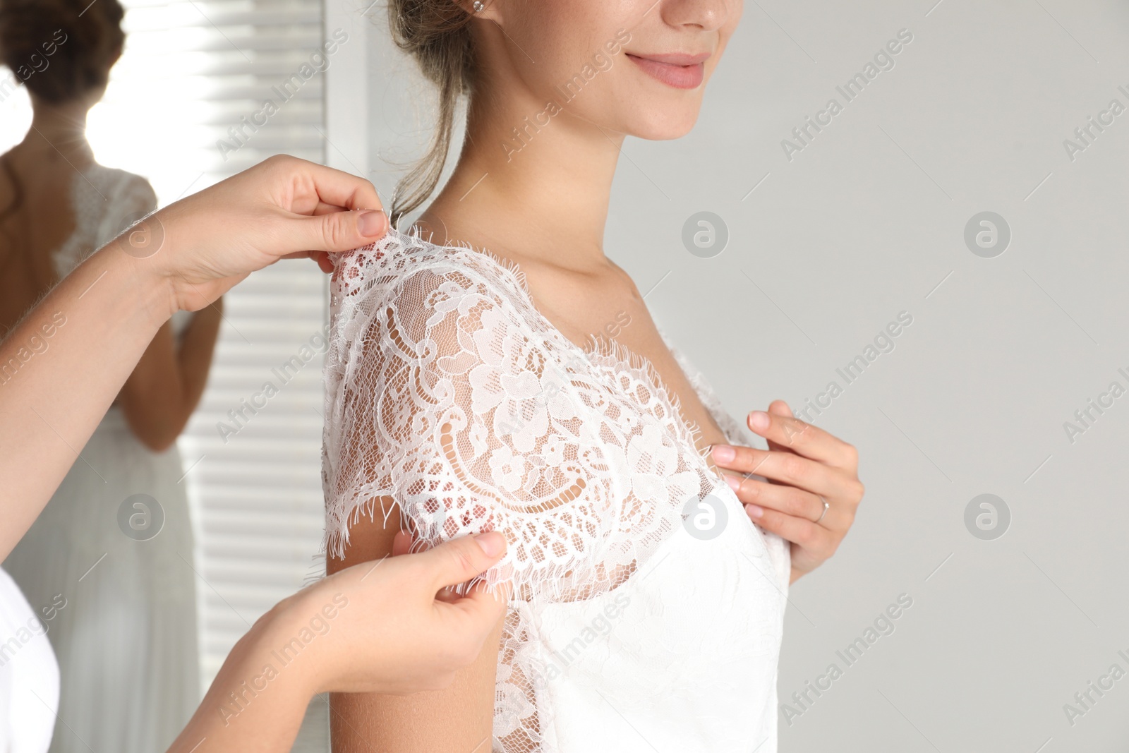 Photo of Woman helping bride to put on wedding dress indoors, closeup
