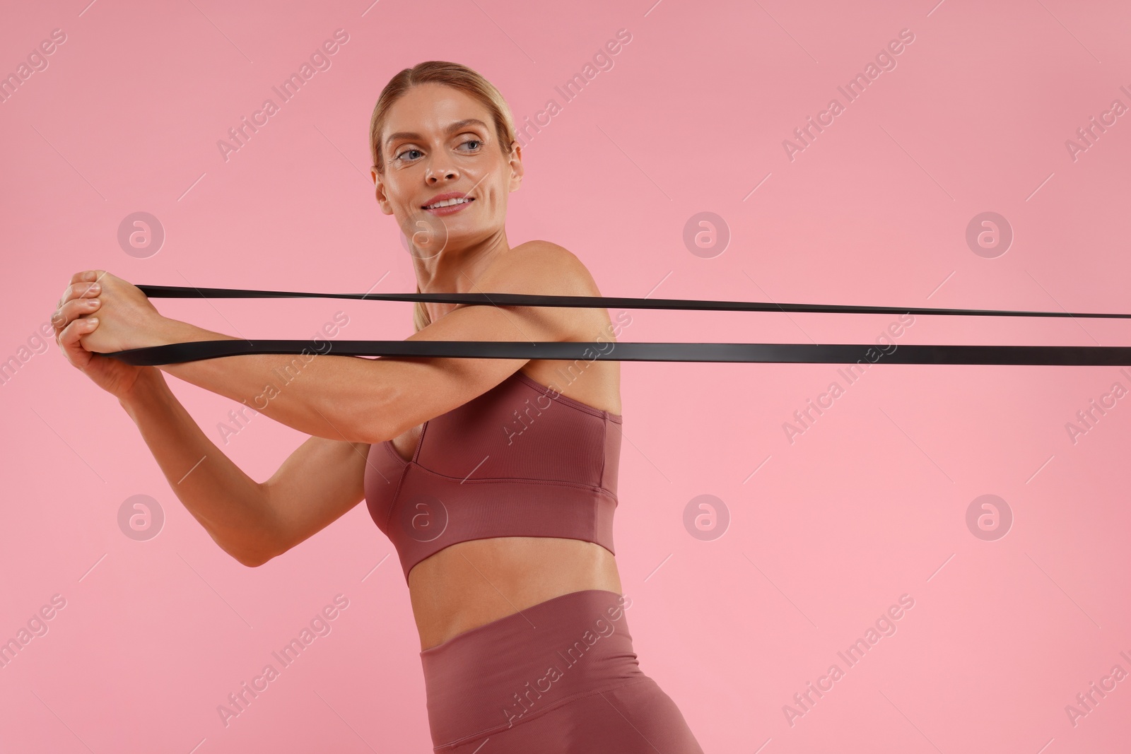 Photo of Woman exercising with elastic resistance band on pink background, low angle view