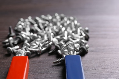 Photo of Magnet attracting screws on dark grey wooden background, closeup