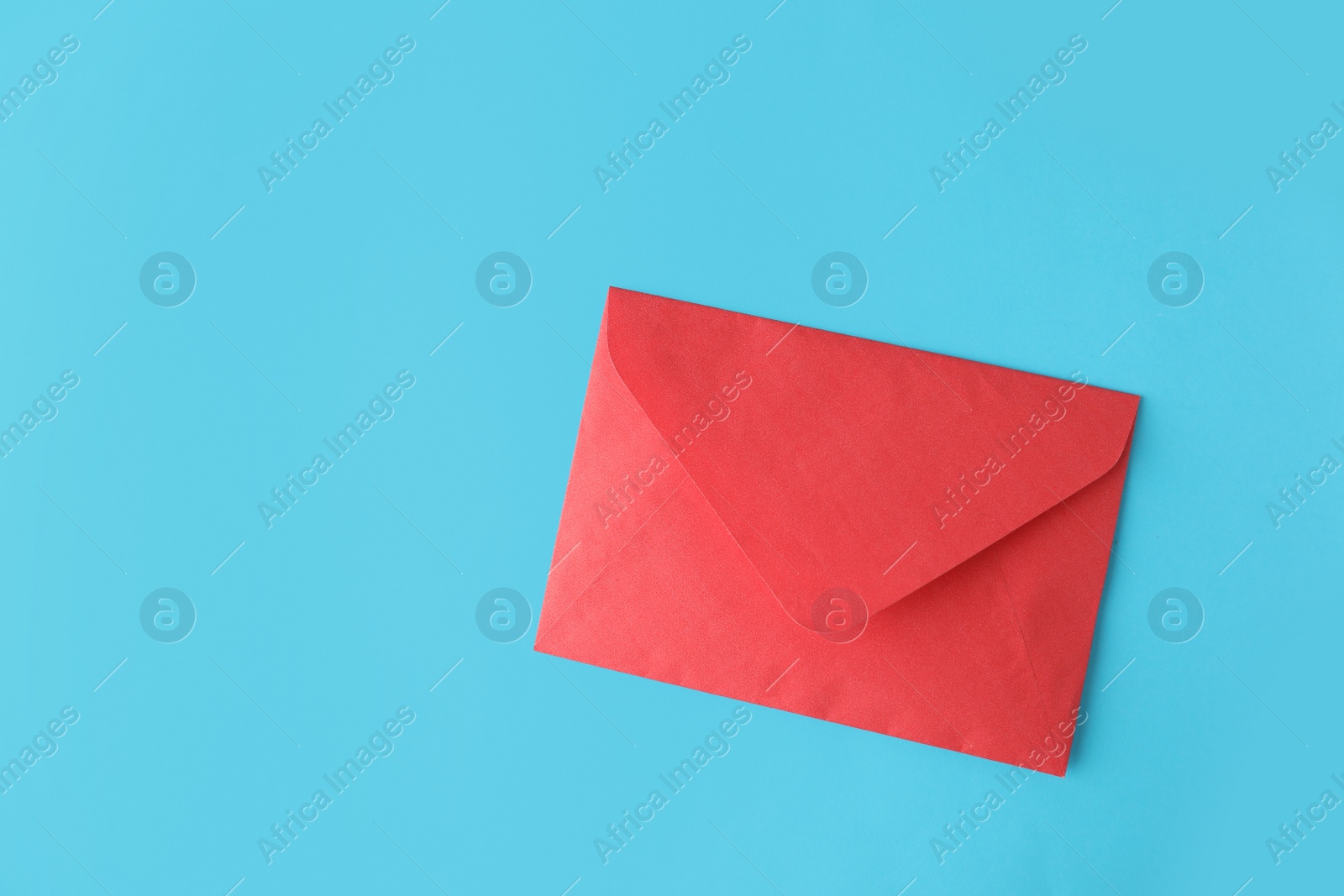 Photo of Red paper envelope on light blue background, top view. Space for text