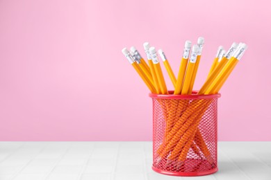 Photo of Many sharp pencils in holder on light table against pink background, space for text