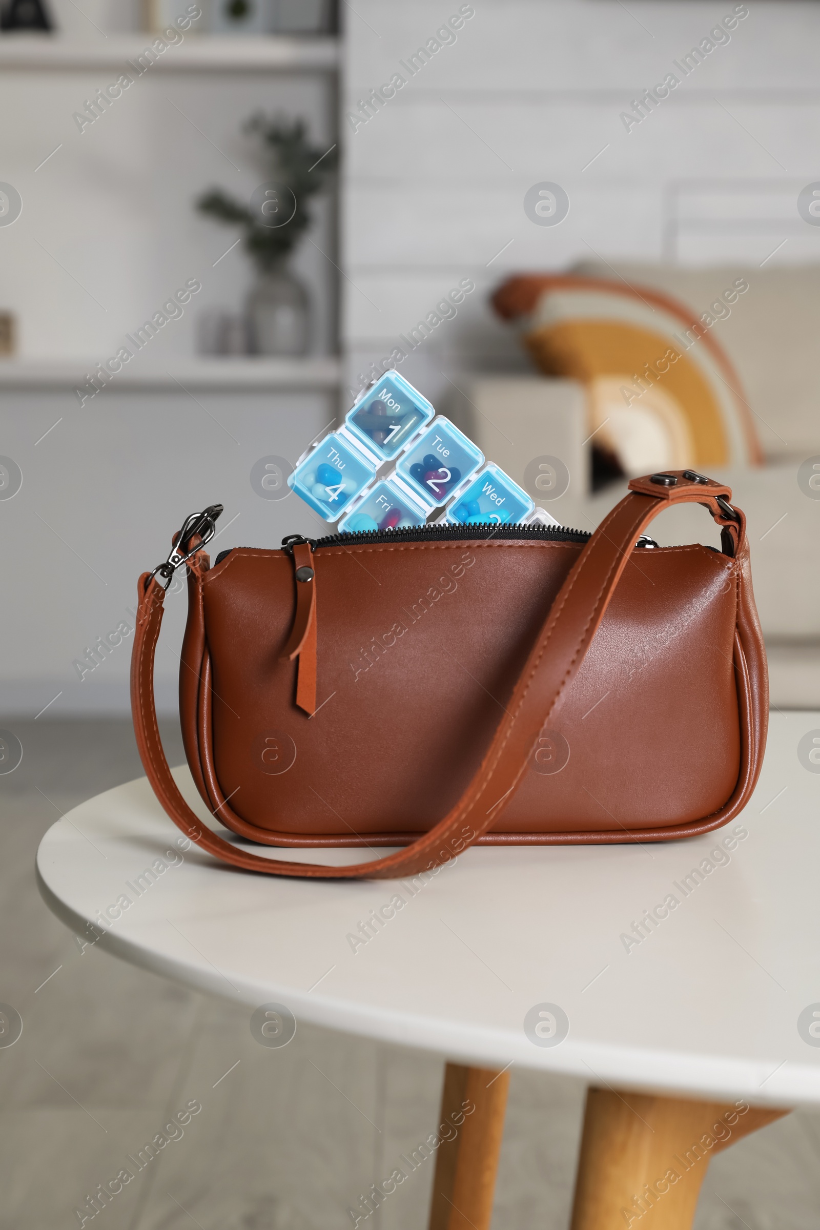 Photo of Stylish women's bag with plastic pill box on white table in room