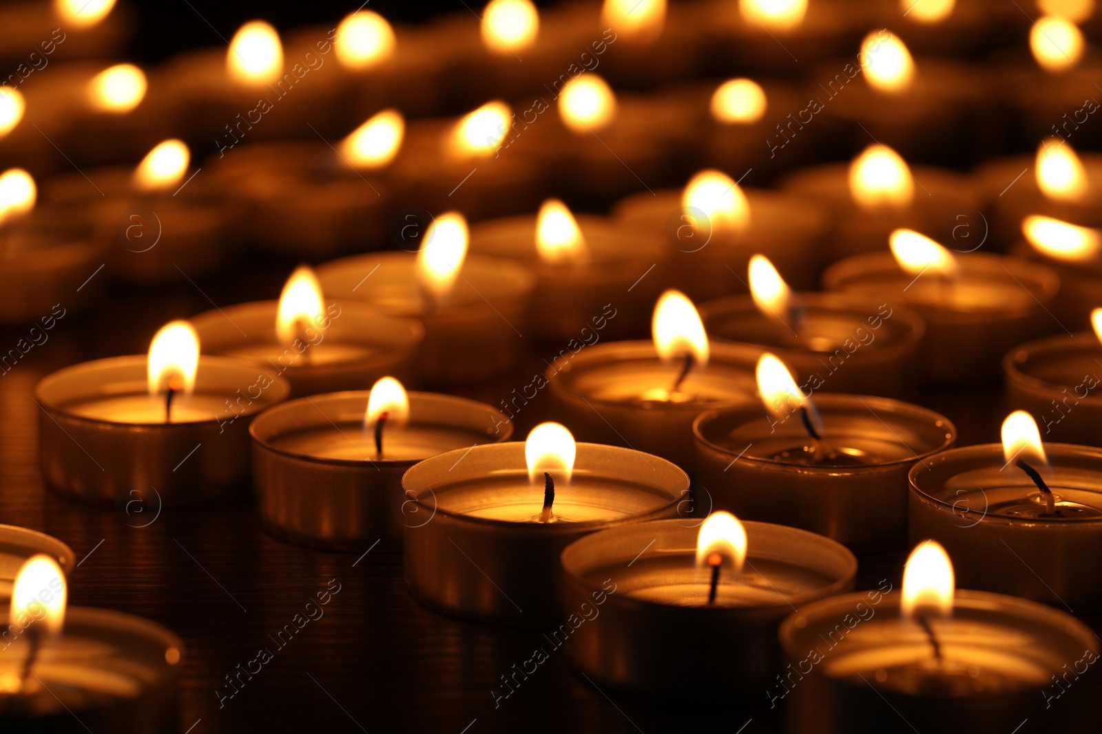 Photo of Burning candles on wooden table in darkness, closeup