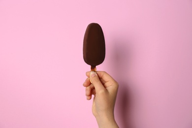 Woman holding delicious ice cream with chocolate against color background