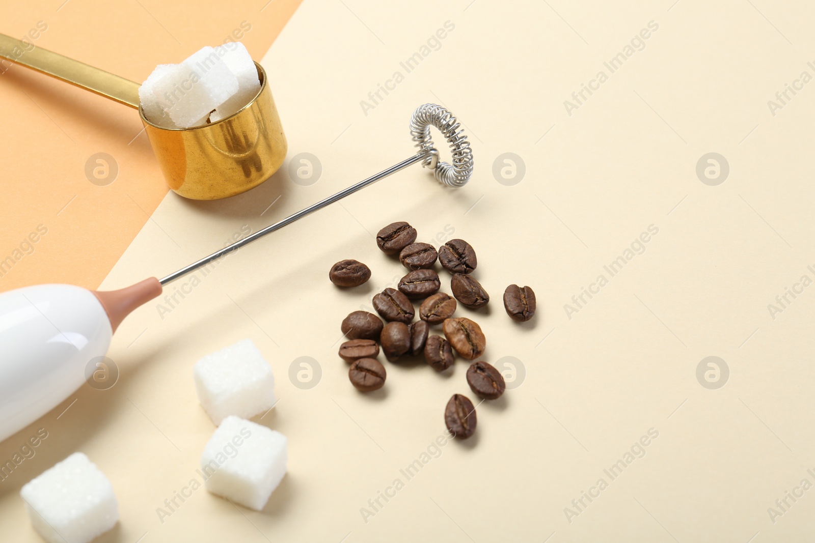 Photo of Milk frother wand, coffee beans and sugar cubes on color background, space for text