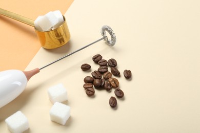 Milk frother wand, coffee beans and sugar cubes on color background, space for text