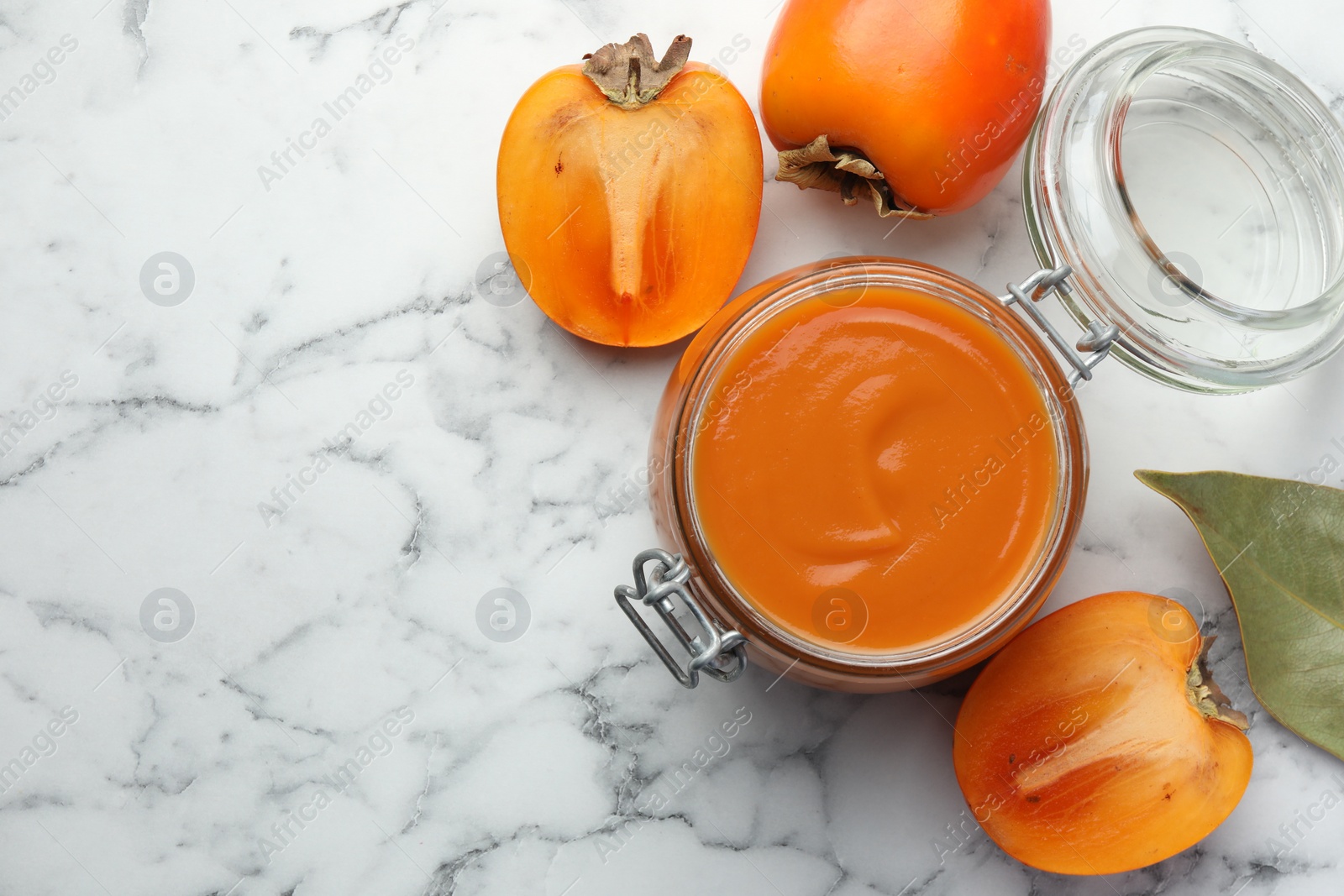 Photo of Delicious persimmon jam and fresh fruits on white marble table, flat lay. Space for text