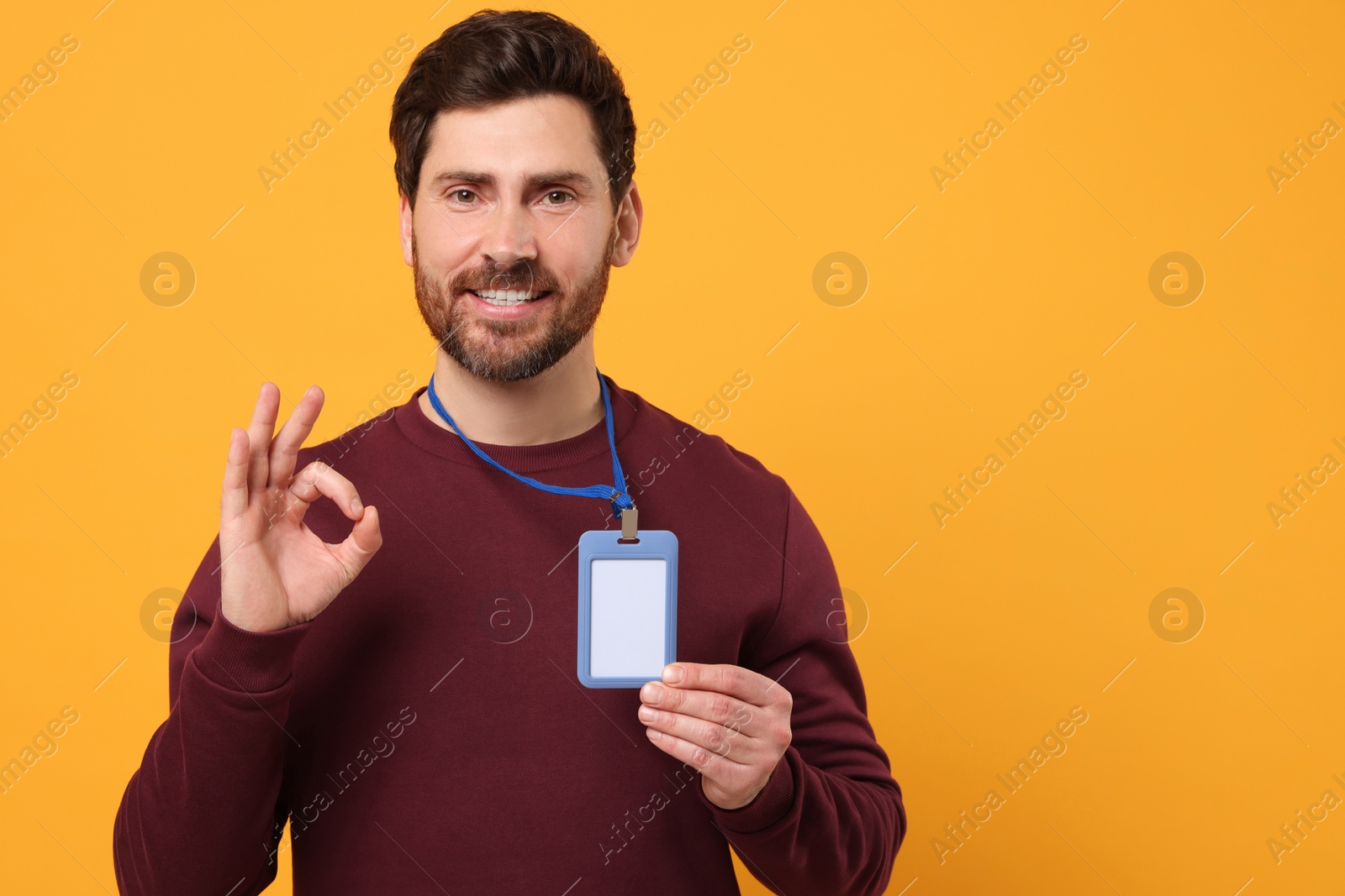 Photo of Smiling man with VIP pass badge showing OK gesture on orange background, space for text
