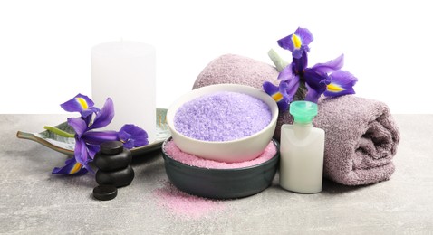 Photo of Different types of sea salt, rolled towel, spa stones, candle and flowers on grey table against white background