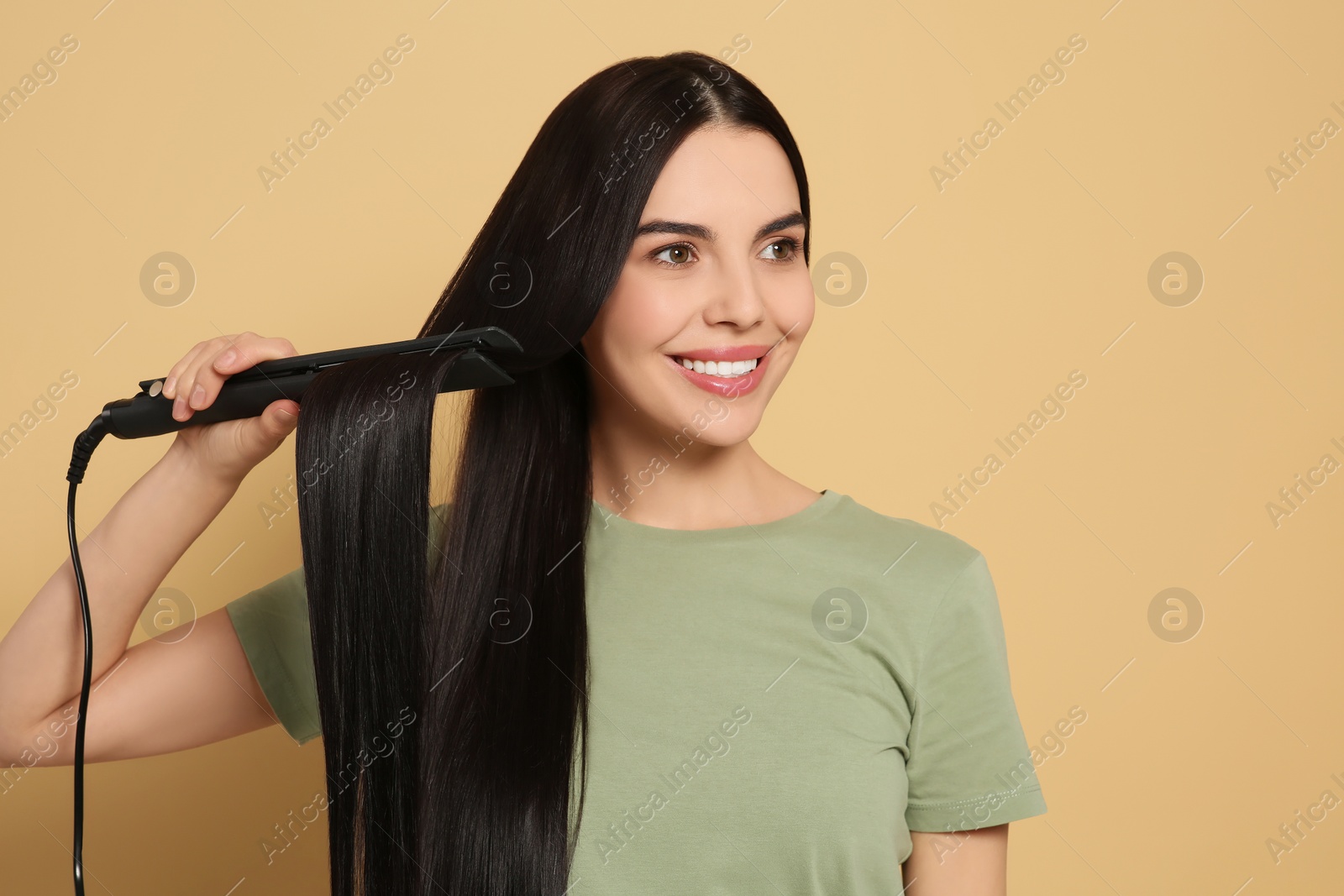 Photo of Beautiful happy woman using hair iron on beige background