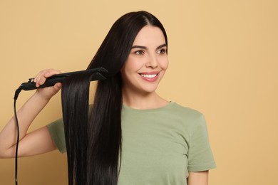 Beautiful happy woman using hair iron on beige background