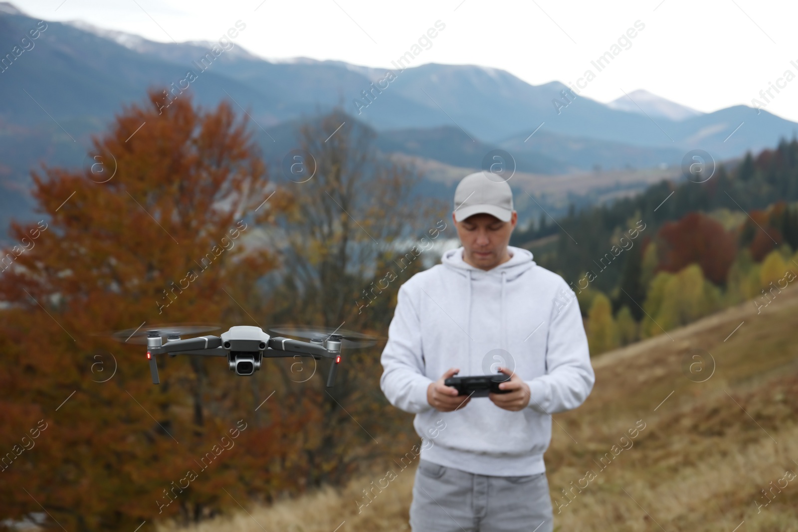Photo of Young man operating modern drone with remote control in mountains