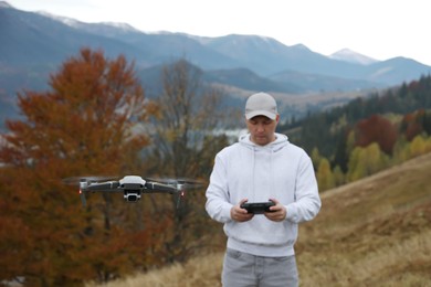 Photo of Young man operating modern drone with remote control in mountains