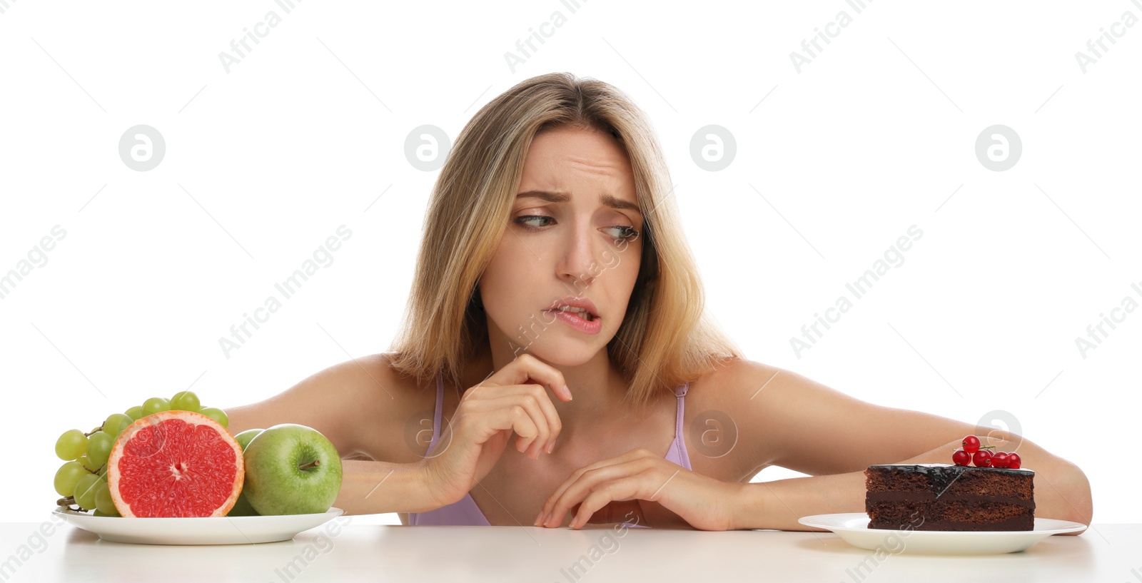 Photo of Woman choosing between cake and healthy fruits at table on white background