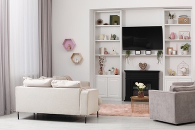 Stylish room interior with beautiful fireplace, TV set, sofa, armchair and shelves with decor