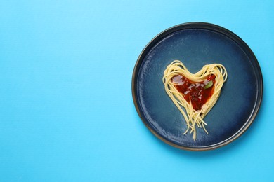 Photo of Heart made with spaghetti and sauce on light blue background, top view. Space for text