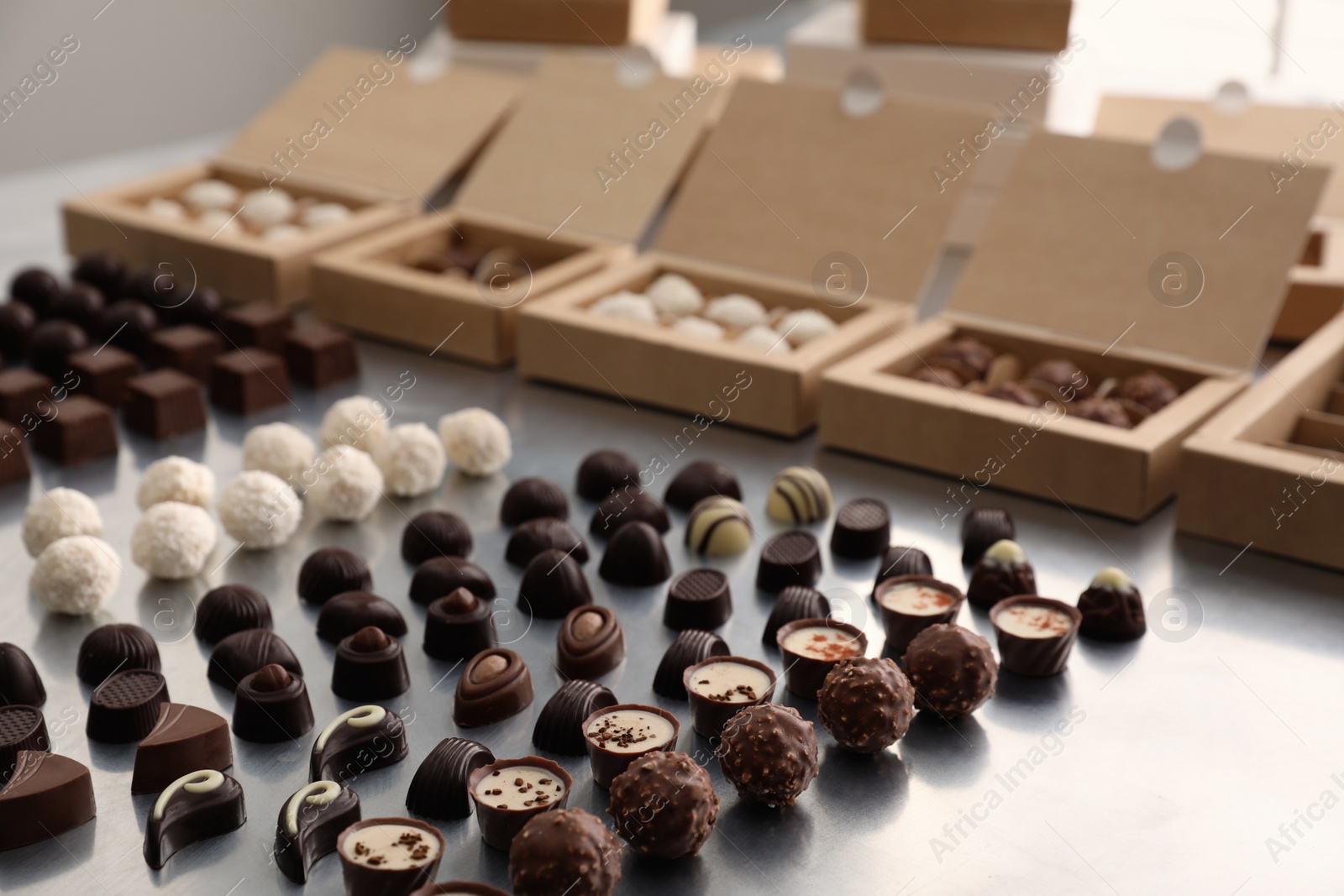 Photo of Different delicious chocolate candies and boxes on white table. Production line