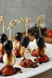 Tasty canapes with black olives, mozzarella and cherry tomatoes on light wooden table, closeup