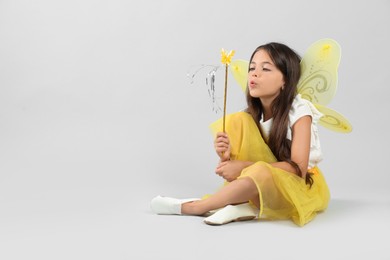 Photo of Cute little girl in fairy costume with yellow wings and magic wand on light background. Space for text