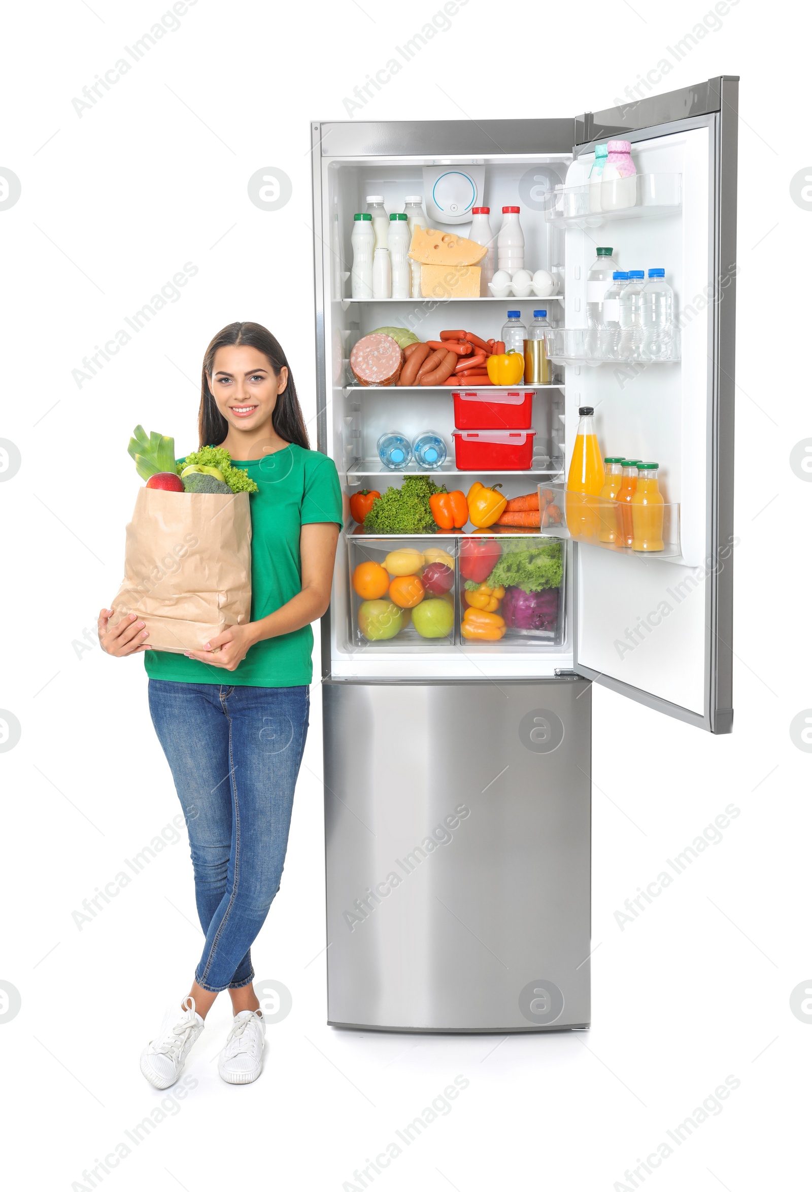 Photo of Young woman with bag of groceries near open refrigerator on white background