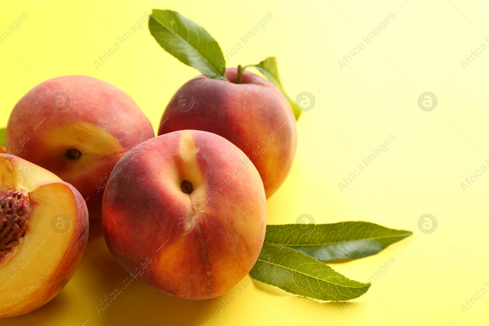 Photo of Fresh ripe peaches and green leaves on yellow background, closeup. Space for text