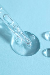 Photo of Glass pipette and transparent liquid on light blue background, closeup