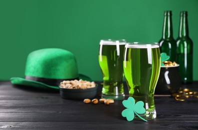Photo of St. Patrick's day party. Green beer, leprechaun hat, pot of gold, pistachios and decorative clover leaf on wooden table. Space for text