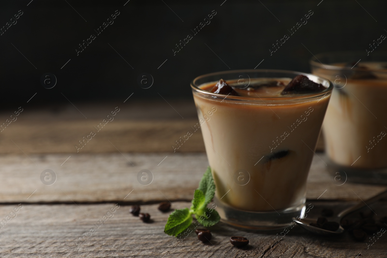 Photo of Glasses of delicious iced coffee with milk, beans and mint on wooden table, space for text