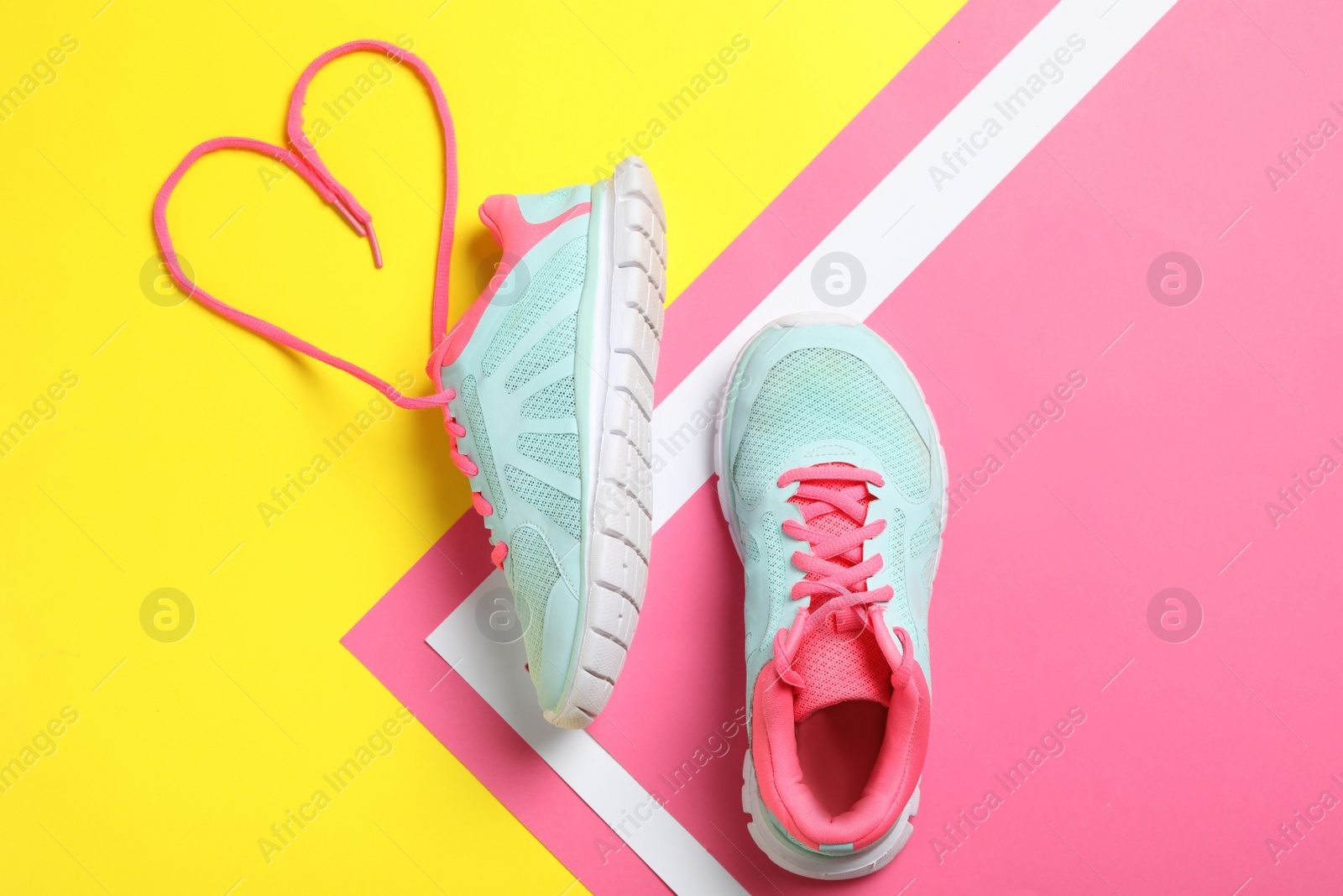 Photo of Stylish sneakers and shoe lace in shape of heart on color background, flat lay