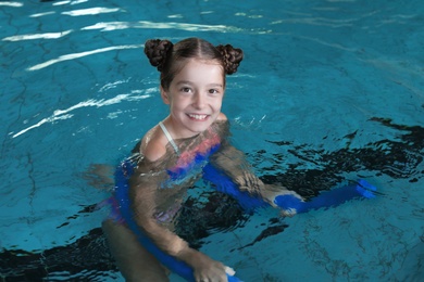 Photo of Little girl with swimming noodle in indoor pool