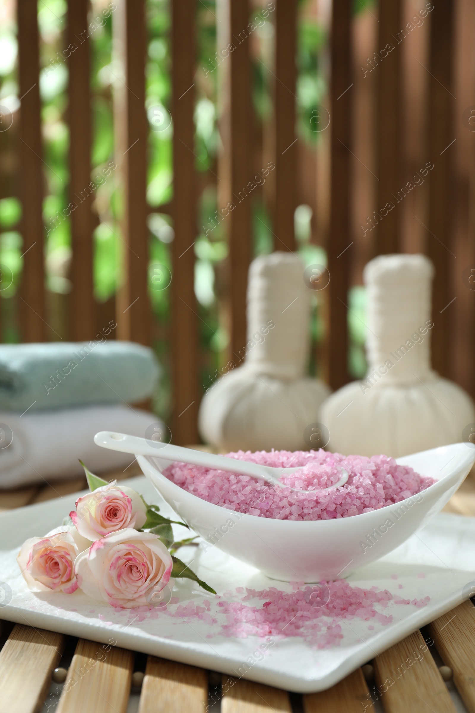 Photo of Bowl of pink sea salt and beautiful roses on wooden table, space for text