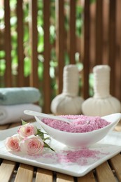 Bowl of pink sea salt and beautiful roses on wooden table, space for text