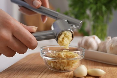 Photo of Woman squeezing garlic with press at wooden table indoors, closeup