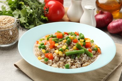 Tasty pearl barley porridge with vegetables on light textured table, closeup