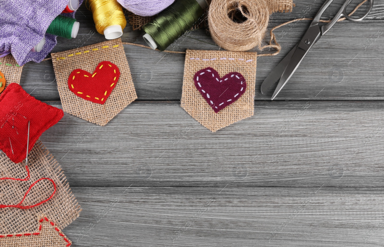 Photo of Bunting flags made with burlap fabric and sewing tools on grey wooden table, flat lay. Space for text