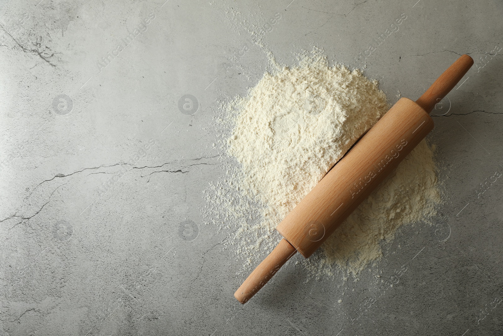 Photo of Flour and rolling pin on grey table, top view. Space for text