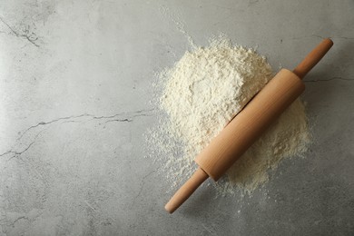 Photo of Flour and rolling pin on grey table, top view. Space for text