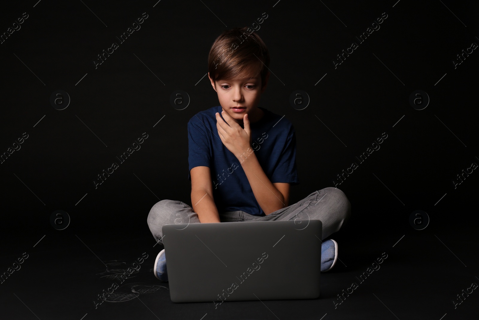 Photo of Shocked child with laptop on black background. Danger of internet