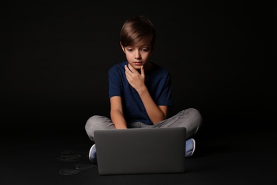 Photo of Shocked child with laptop on black background. Danger of internet