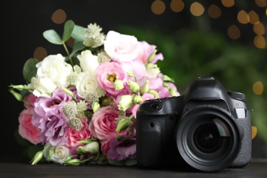Photo of Modern camera and bouquet on black wooden table. International Photographer's day