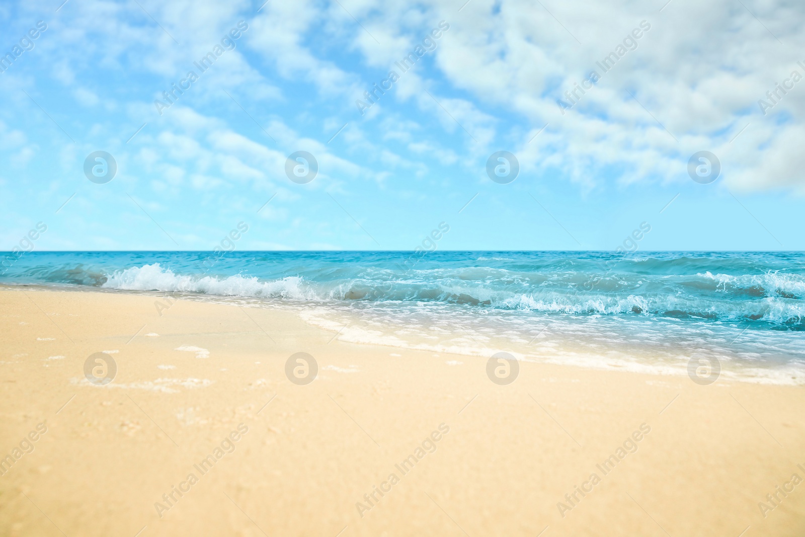 Image of Ocean waves rolling on sandy beach under blue sky with clouds