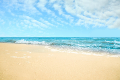 Image of Ocean waves rolling on sandy beach under blue sky with clouds