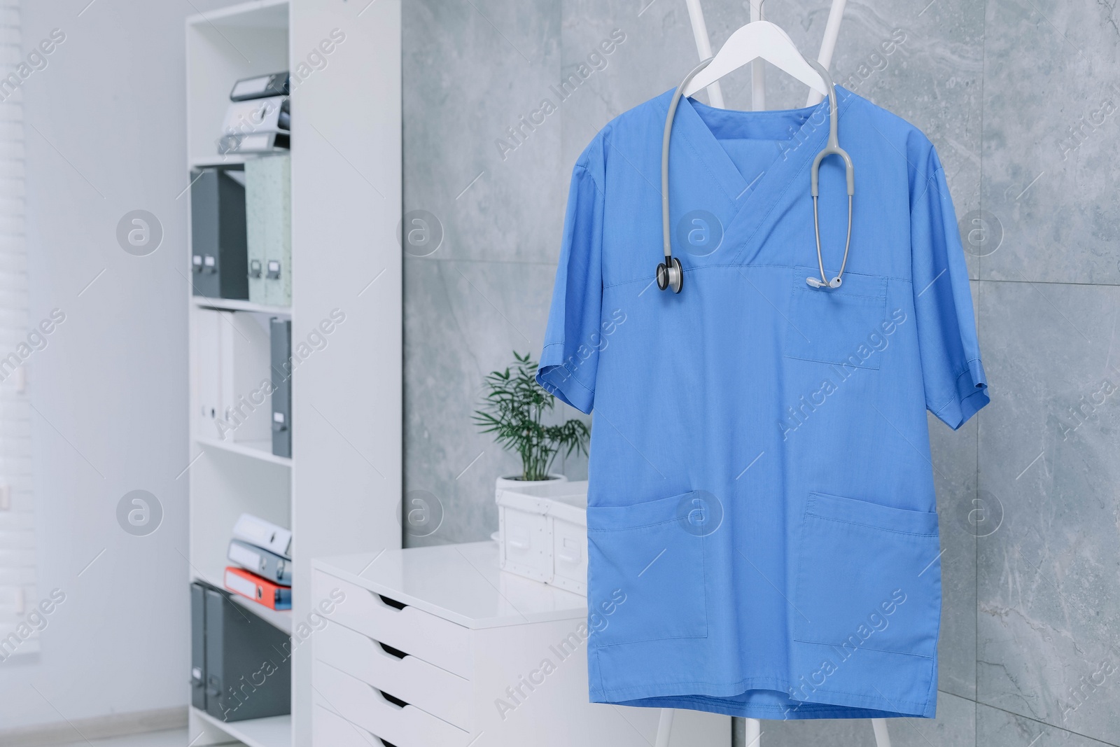 Photo of Blue medical uniform and stethoscope hanging on rack in clinic. Space for text