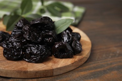 Photo of Tasty dried prunes and green leaf on wooden table, closeup