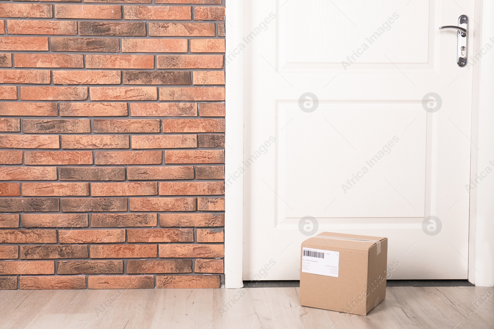 Photo of Cardboard parcel box on floor near apartment entrance. Mockup for design