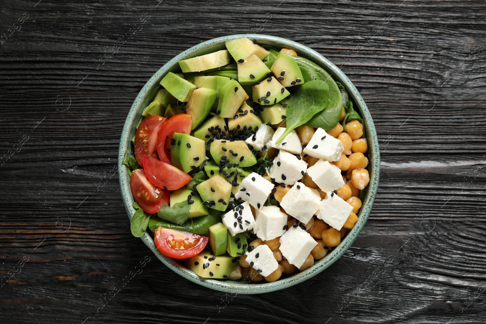Photo of Delicious avocado salad with feta cheese on black wooden table, top view