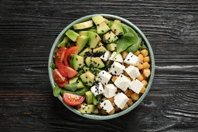 Delicious avocado salad with feta cheese on black wooden table, top view