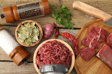 Photo of Meat grinder with beef, garlic, parsley and spices on wooden table, flat lay