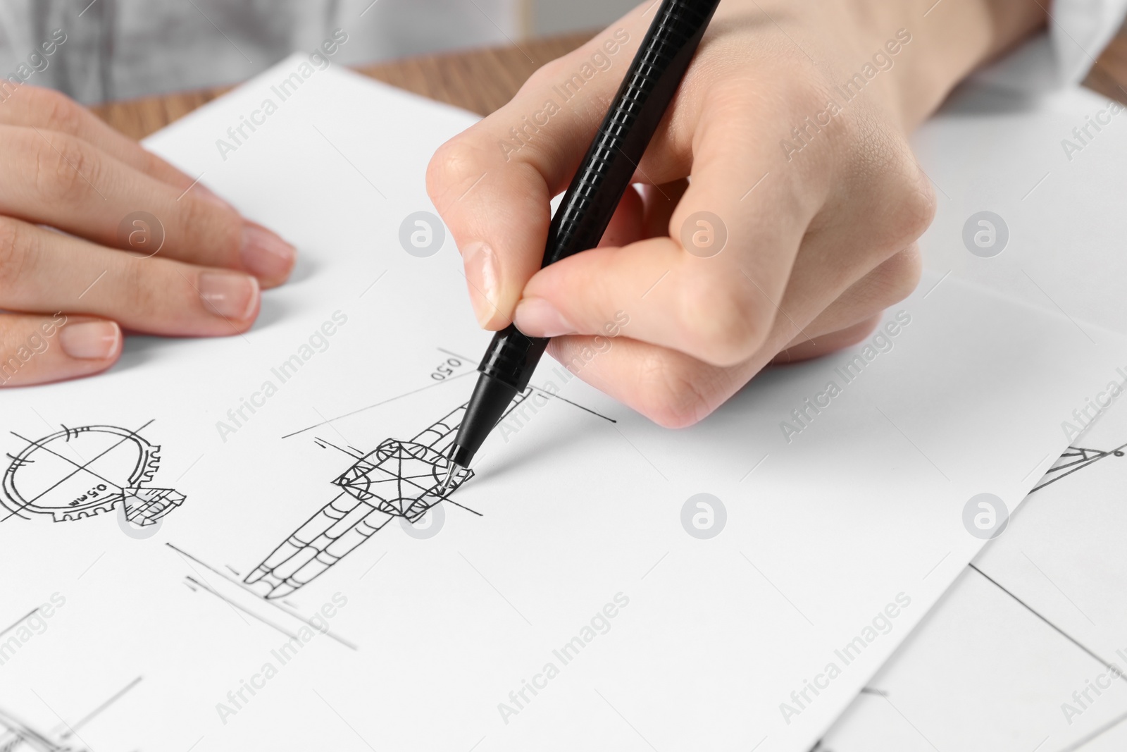 Photo of Jeweler drawing sketch of elegant ring on paper at wooden table, closeup