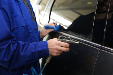 Photo of Worker cleaning automobile with gun and rag at car wash, closeup
